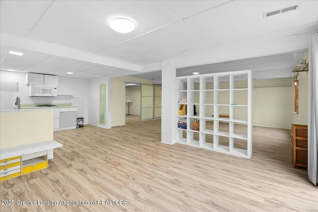 unfurnished living room featuring baseboards, light wood-style floors, visible vents, and a sink