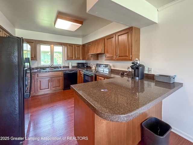 515 N Putnam St Unit B, Williamston, MI 48895 - kitchen featuring black appliances, a peninsula, premium range hood, and brown cabinets