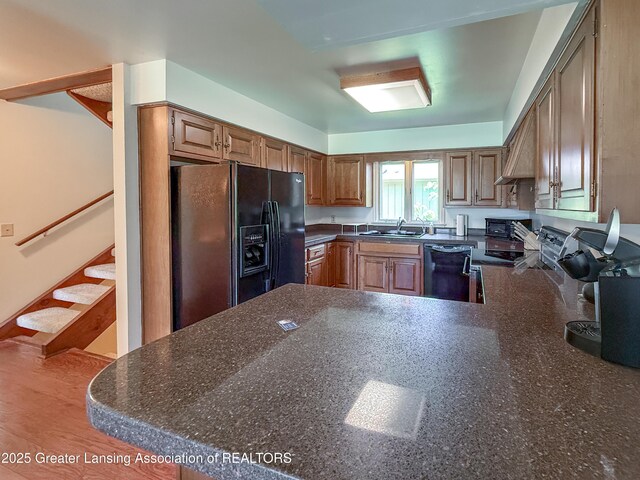 515 N Putnam St Unit B, Williamston, MI 48895 - kitchen with black appliances, a peninsula, a sink, brown cabinetry, and dark stone countertops