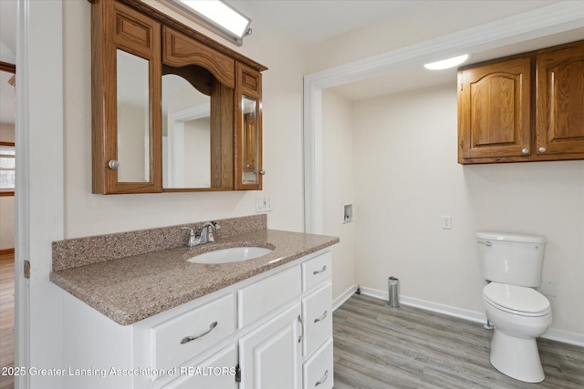 half bath with baseboards, wood finished floors, vanity, and toilet
