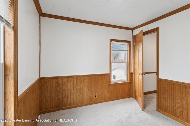 carpeted spare room featuring wainscoting, wooden walls, and crown molding