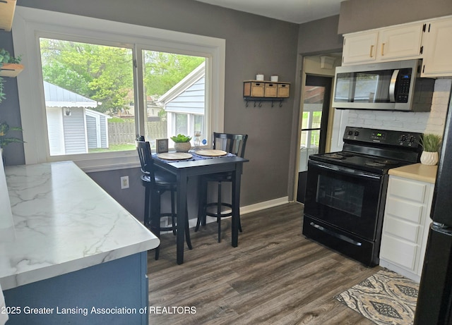 2032 Hillcrest St, Lansing, MI 48910 - kitchen featuring black range with electric stovetop, stainless steel microwave, tasteful backsplash, white cabinets, and dark wood-style floors