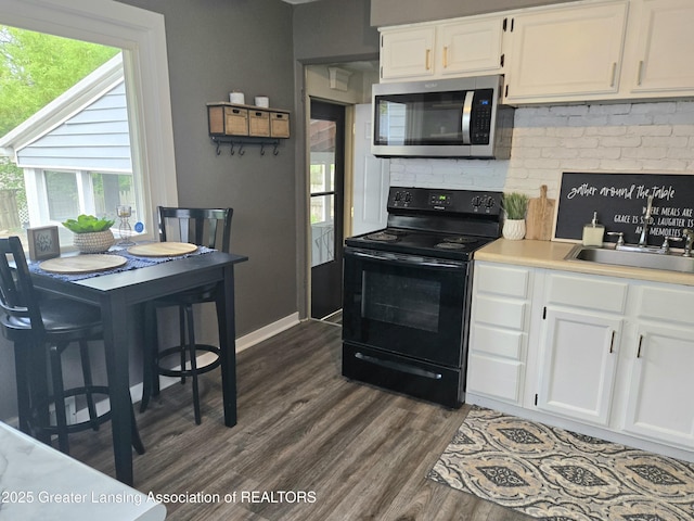 2032 Hillcrest St, Lansing, MI 48910 - kitchen featuring stainless steel microwave, black range with electric stovetop, dark wood-type flooring, and white cabinetry
