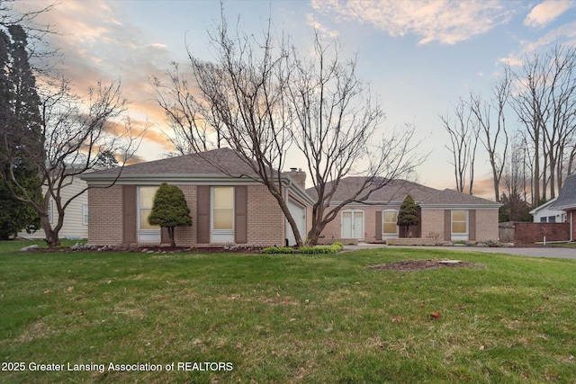 ranch-style house featuring a chimney, brick siding, a yard, and a garage
