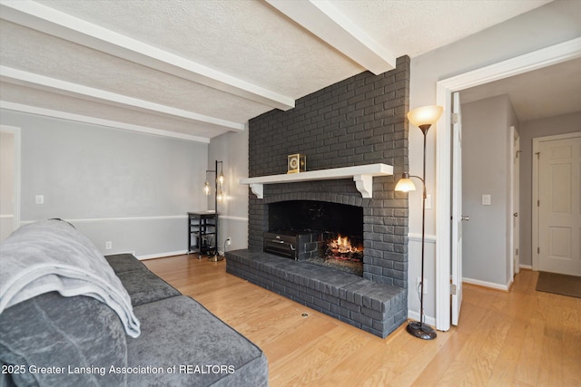 living room featuring wood finished floors, a textured ceiling, a fireplace, baseboards, and beam ceiling
