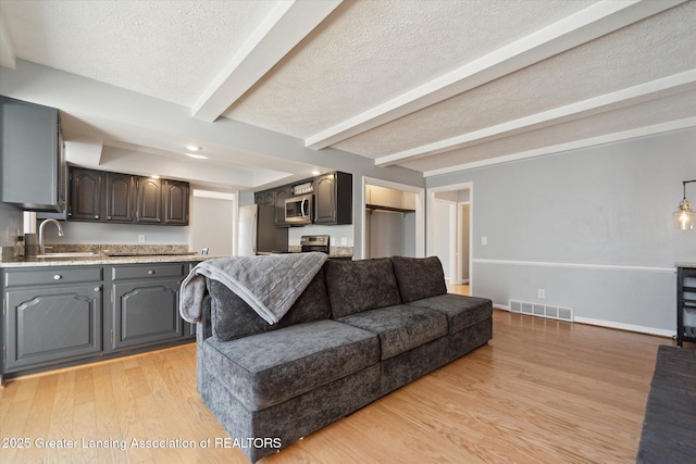 living area with a textured ceiling, light wood-style floors, baseboards, beam ceiling, and visible vents