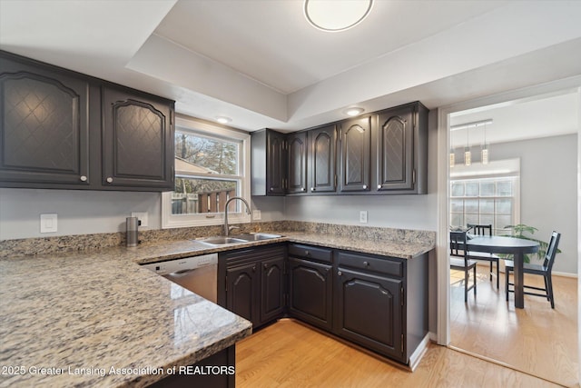 kitchen featuring dishwasher, light stone countertops, a sink, and light wood-style floors
