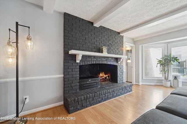 living area with a brick fireplace, wood finished floors, beamed ceiling, baseboards, and a textured ceiling