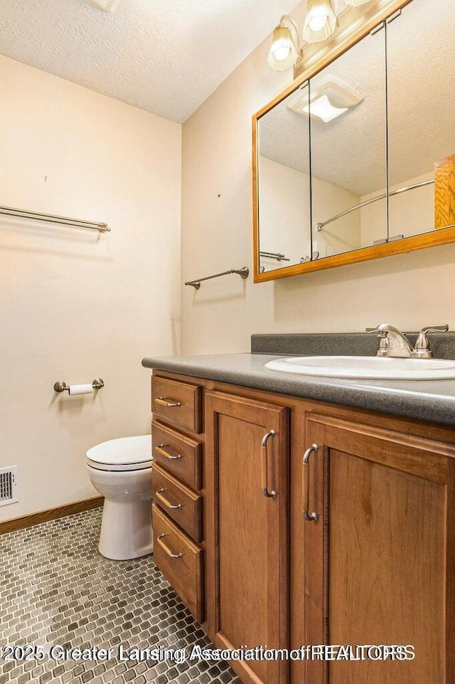 bathroom featuring a textured ceiling, toilet, baseboards, tile patterned flooring, and vanity