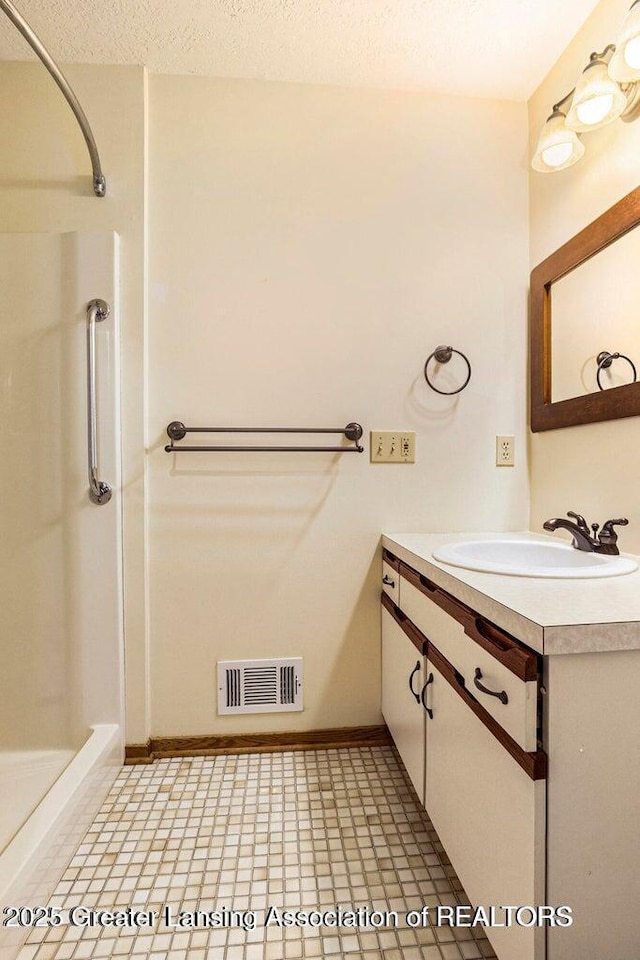 bathroom with a shower stall, baseboards, vanity, and visible vents