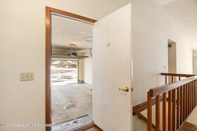 hallway featuring visible vents, an upstairs landing, and a textured ceiling