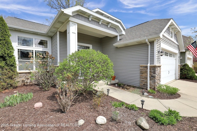 view of front facade featuring concrete driveway, a shingled roof, and stone siding