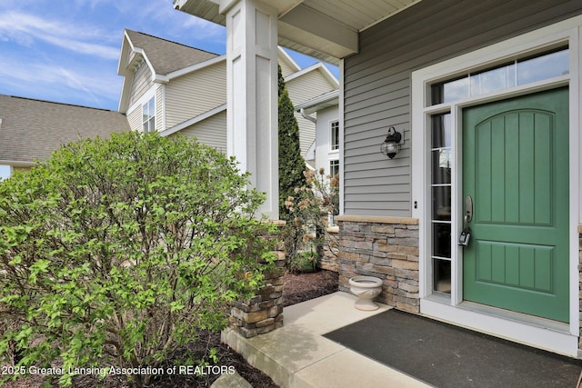 doorway to property featuring roof with shingles and stone siding