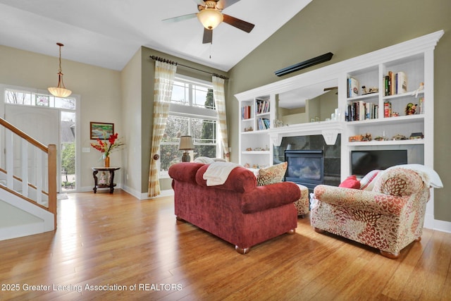 living room with a tiled fireplace, a ceiling fan, plenty of natural light, and wood finished floors