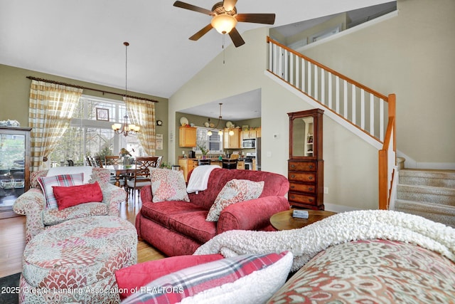living room with high vaulted ceiling, light wood-style flooring, stairway, and ceiling fan with notable chandelier