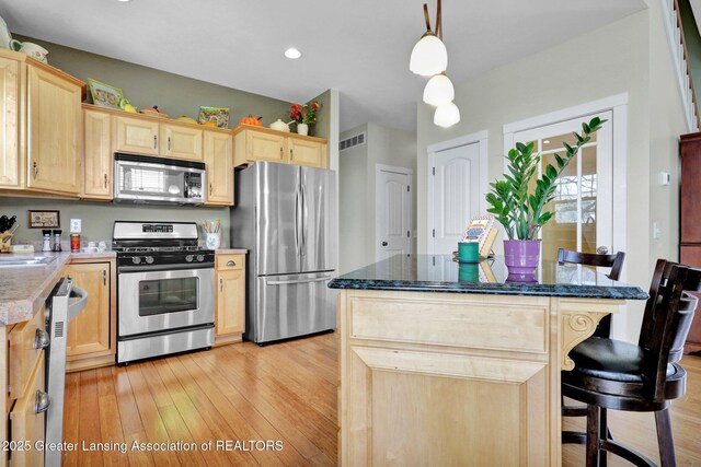 kitchen with a kitchen breakfast bar, visible vents, light brown cabinetry, appliances with stainless steel finishes, and light wood finished floors