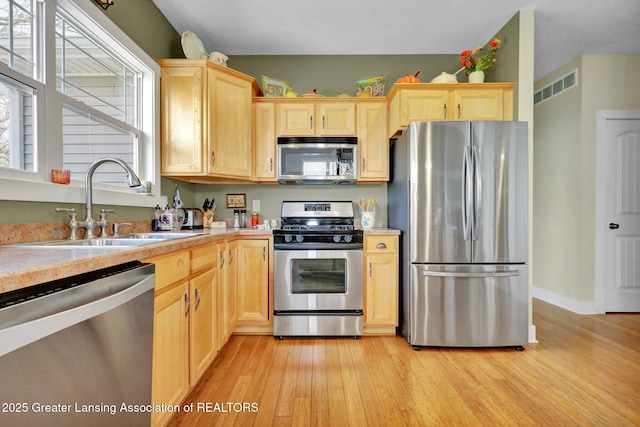 kitchen with light brown cabinetry, appliances with stainless steel finishes, a sink, and light countertops