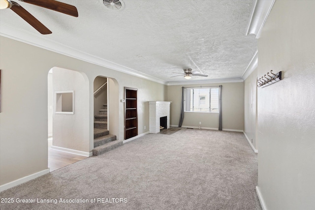 unfurnished living room with crown molding, ceiling fan, a fireplace, carpet, and visible vents