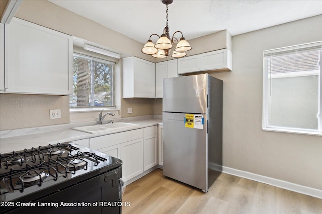 kitchen featuring a sink, black range with gas stovetop, a chandelier, freestanding refrigerator, and white cabinetry