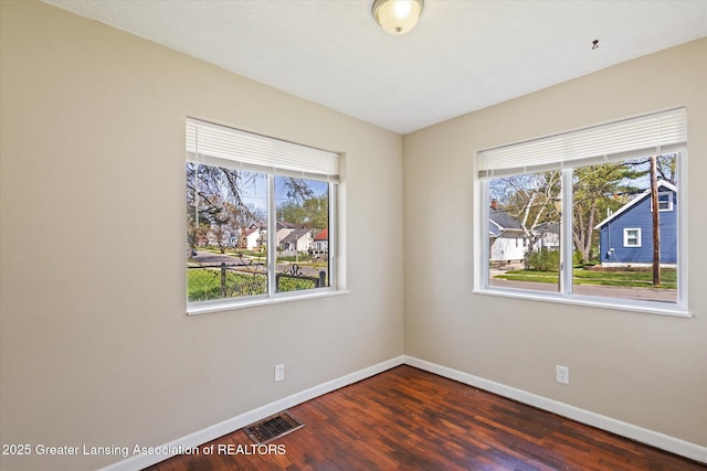 unfurnished room with baseboards, a wealth of natural light, dark wood-style floors, and visible vents