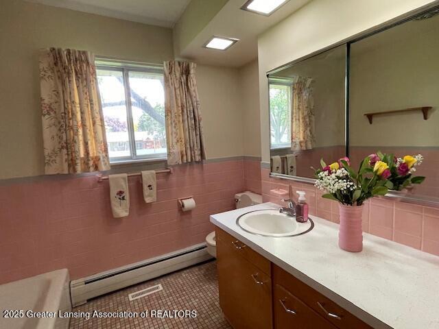 505 S Baker St, Saint Johns, MI 48879 - bathroom with a baseboard radiator, vanity, tile walls, a bathtub, and toilet