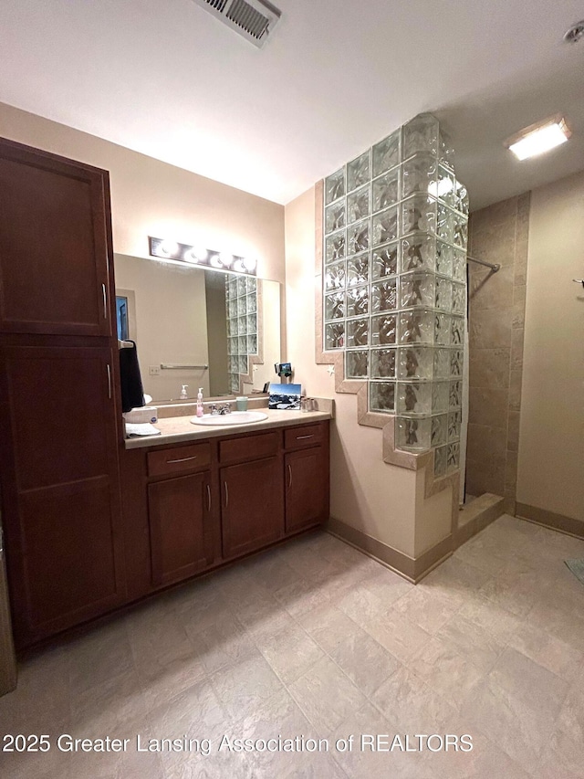 bathroom with baseboards, visible vents, vanity, and a walk in shower