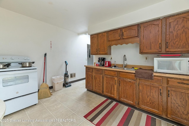 kitchen with white appliances, a sink, brown cabinetry, light countertops, and light tile patterned floors
