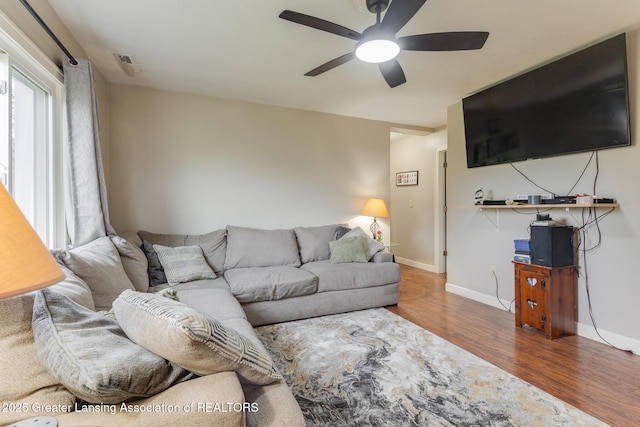 living room featuring visible vents, baseboards, a ceiling fan, and wood finished floors