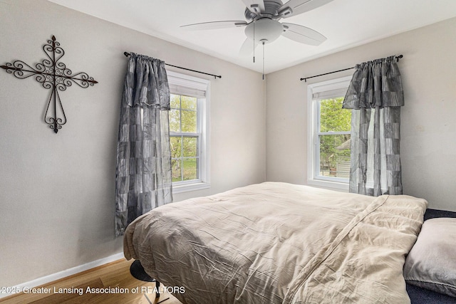 bedroom with a ceiling fan, multiple windows, wood finished floors, and baseboards
