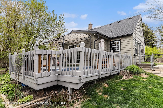 back of house with a chimney, fence, a wooden deck, and a shingled roof