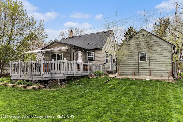 rear view of house with a lawn, roof with shingles, a chimney, and a deck
