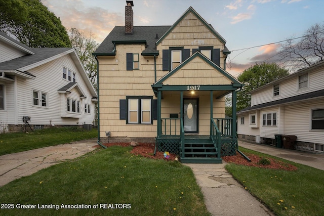 view of front of home featuring roof with shingles, a chimney, a yard, and a porch