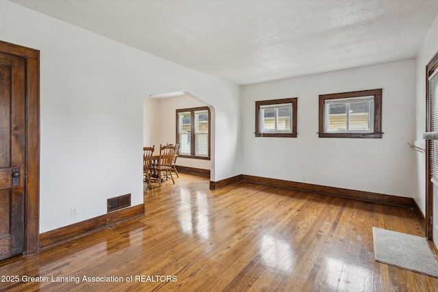 spare room featuring arched walkways, baseboards, hardwood / wood-style flooring, and visible vents