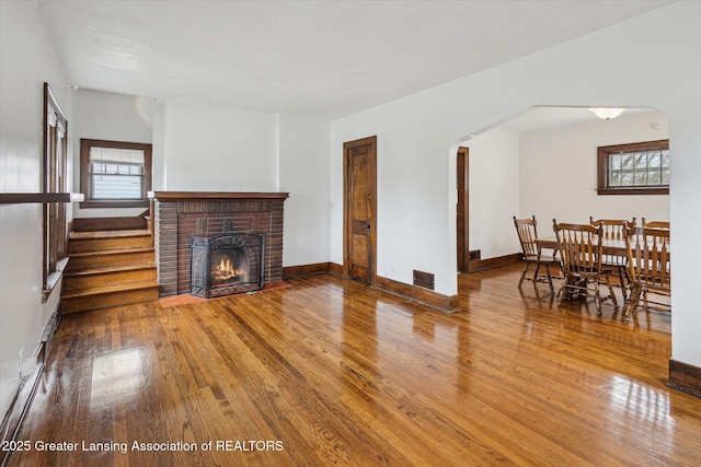 living area featuring arched walkways, a fireplace, a healthy amount of sunlight, and hardwood / wood-style floors