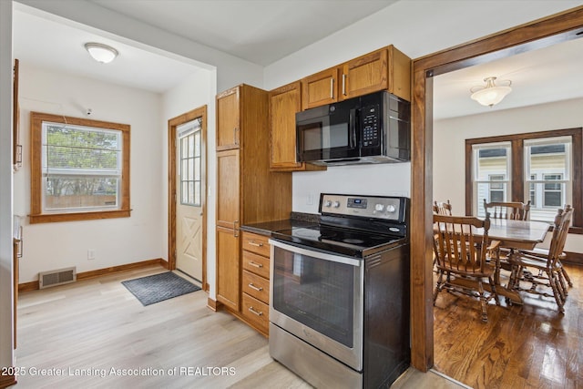 kitchen featuring stainless steel electric range oven, black microwave, visible vents, and light wood-style floors