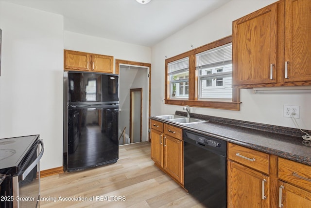 kitchen featuring dark countertops, brown cabinets, a sink, light wood finished floors, and black appliances