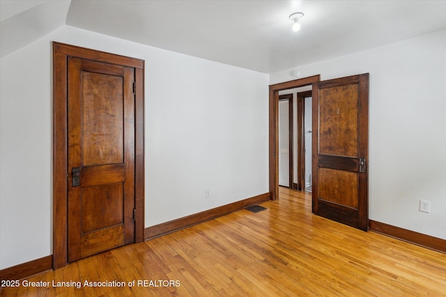empty room with visible vents, light wood finished floors, and baseboards