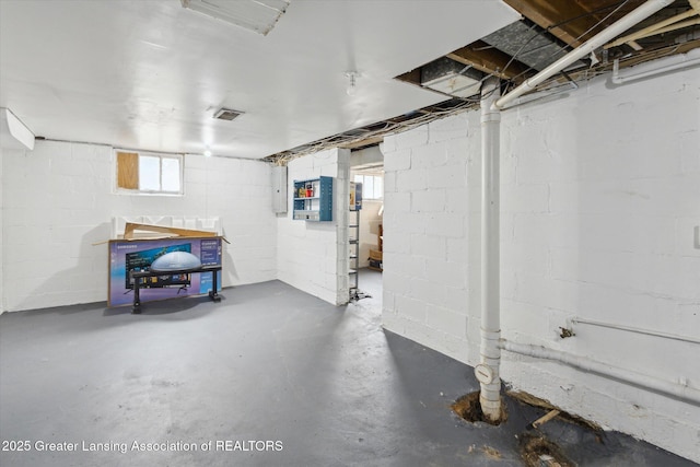 below grade area with concrete block wall, electric panel, and visible vents