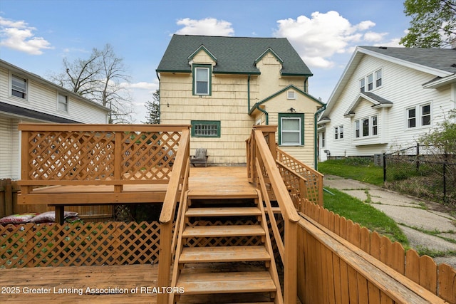exterior space with fence, a wooden deck, a shingled roof, and stairs