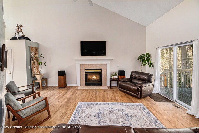 living area featuring light wood-type flooring, baseboards, visible vents, high vaulted ceiling, and a fireplace