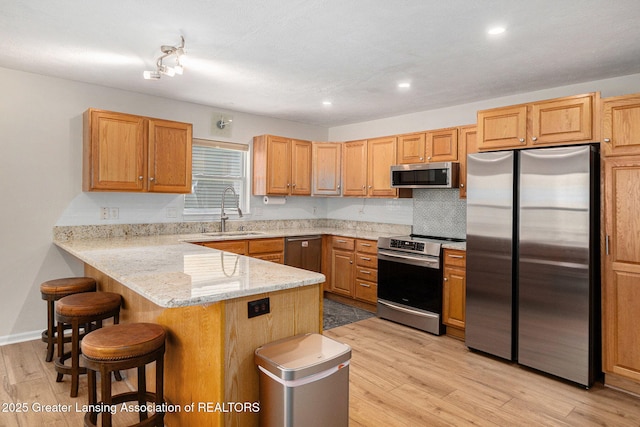 kitchen featuring a sink, light wood-style floors, a kitchen breakfast bar, a peninsula, and appliances with stainless steel finishes