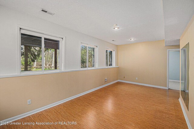 spare room with baseboards, a textured ceiling, visible vents, and light wood-style flooring