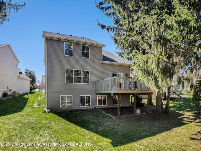 rear view of property with cooling unit, a lawn, a deck, and roof with shingles