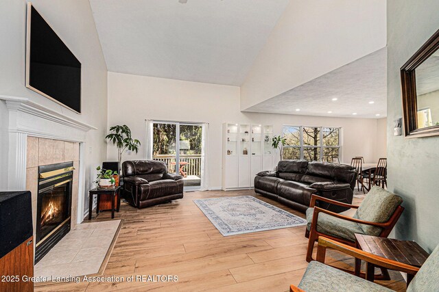 living area with a fireplace, a wealth of natural light, wood finished floors, and high vaulted ceiling