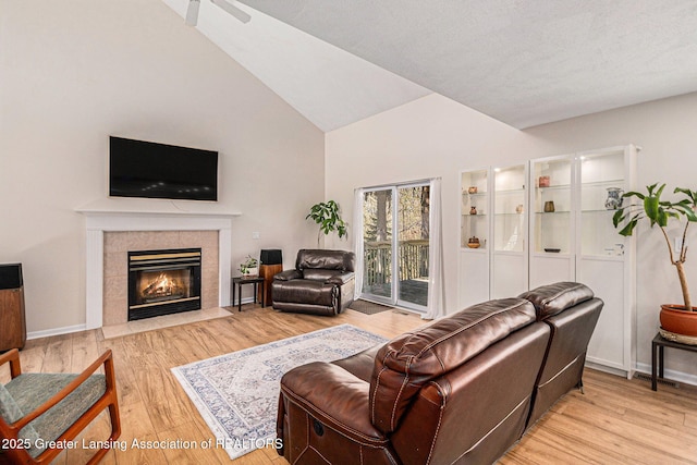 living room featuring light wood-type flooring, a tiled fireplace, and high vaulted ceiling