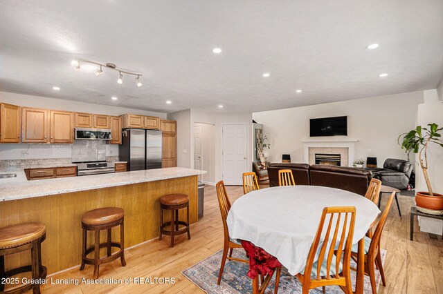 dining space with light wood-style flooring, recessed lighting, and a warm lit fireplace