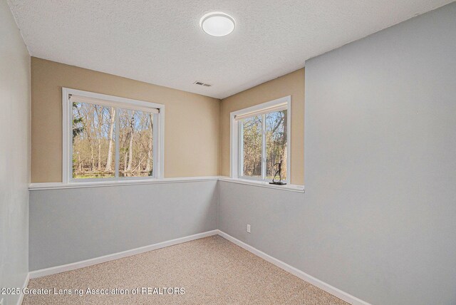carpeted empty room featuring baseboards, a textured ceiling, and visible vents