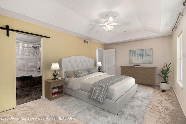 carpeted bedroom with ensuite bath, a barn door, visible vents, a raised ceiling, and a ceiling fan