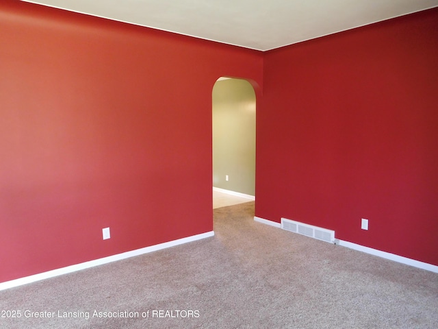 carpeted empty room featuring arched walkways, visible vents, and baseboards