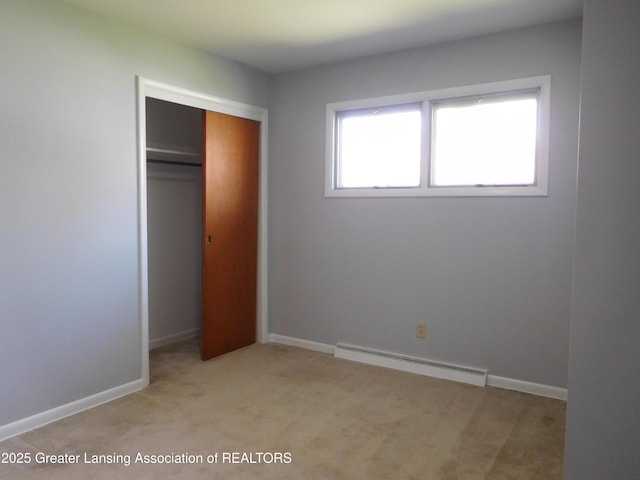 unfurnished bedroom with baseboards, light colored carpet, a closet, and a baseboard radiator